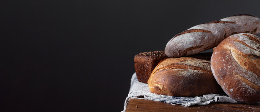 Loafs Of Traditional And Natural Bread On A Wooden Table With Linen Towel. Assortment Of Artisanal Bread. Healthy Food Concept. Panoramic Frame With Free Space For Input Text.