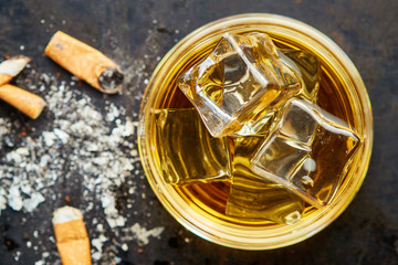Cigarette butts with glass of whiskey on black rustic background. Top view with copy space