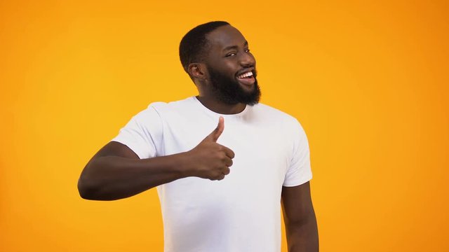 African american man giving thumbs up and winking, isolated on yellow background