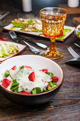 Fresh salad with strawberry, spinach and cheese in a bowl on wooden background. Served restaurant table with cutlery. Selective focus, Vertical card. Copy space.