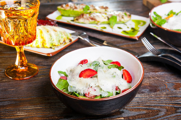 Fresh salad with strawberry, spinach and cheese in a bowl on wooden background. Served restaurant table with cutlery. Selective focus, Copy space.