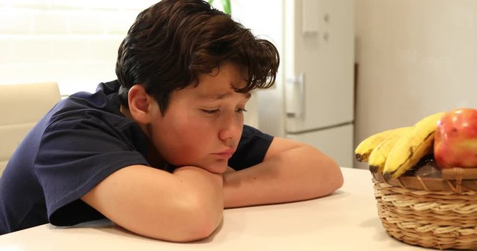 Portrait of a unhappy preteen boy sitting in the kitchen alone.