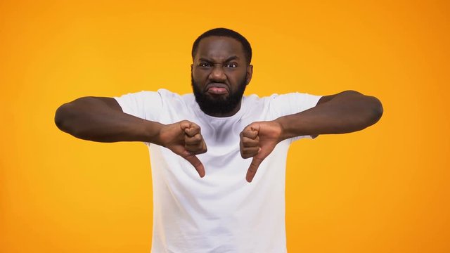 Confident african american man giving harsh thumbs down on yellow background