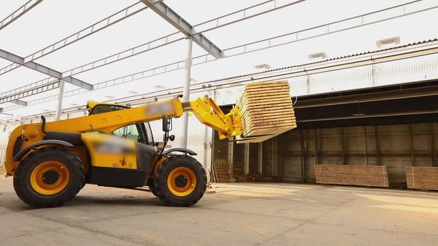 A bulldozer delivers firewood to the warehouse, forklift in a factory, a large yellow forklift in a factory delivers a wooden beam to the warehouse