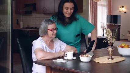 Caring nurse showing a digital tablet to an elderly woman in a nursing home. Hendheld movement slow motion 4k