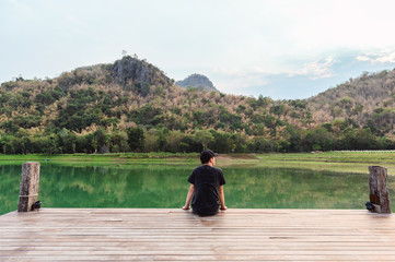 Man relaxing on wooden bridge in green lake