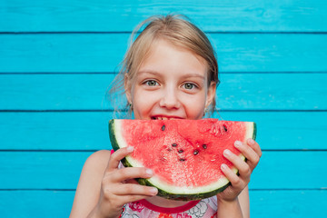 Little girl eating a ripe juicy watermelon over blue plank wall background