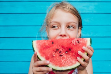 Little girl eating a ripe juicy watermelon over blue plank wall background - Powered by Adobe