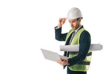 male engineer in hardhat and safety vest holding blueprint and using laptop, isolated on white