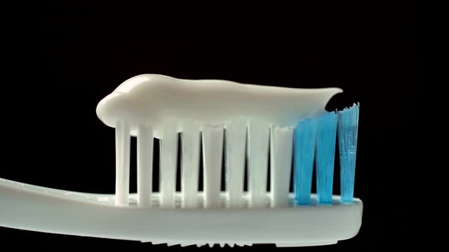 Putting toothpaste on toothbrush on black background, hygiene, cleaning teeth. Extreme close-up