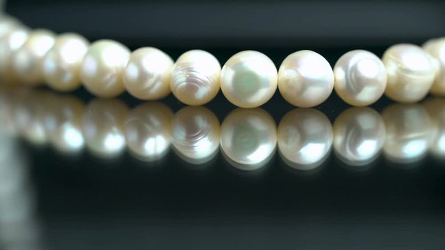 Macro shot of white pearl necklace on reflective surface, jewelry store. Extreme close-up