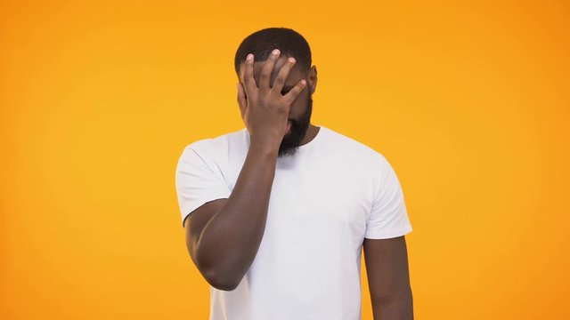 Disappointed afro american male doing facepalm gesture against yellow background