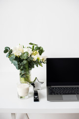 Hipster bloggers work place, laptop and flowers on white tabletop
