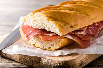 Spanish serrano ham sandwich on wooden table. Close up
