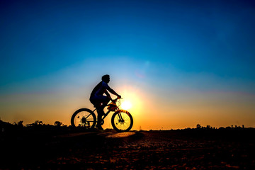 Silhouette of cyclist in sunset background.