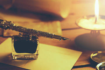 old quill pen and inkwell on brown wooden table with candle