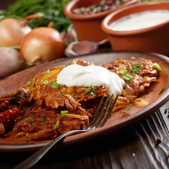 Homemade tasty potato pancakes in clay dish with sun-dried tomatoes and sour cream