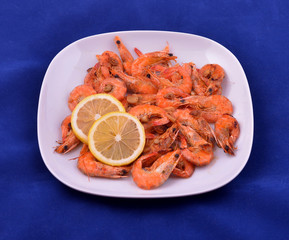 Red shrimps cooked with butter, garlic and lemon on white plate and blue background
