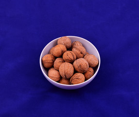 Walnuts in white ceramic bowl on blue background