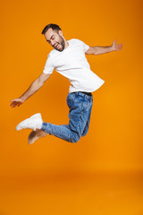 Fototapeta na wymiar Full length photo of positive guy in t-shirt and jeans jumping and having fun, isolated over yellow background