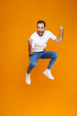 Fototapeta na wymiar Full length photo of young guy in t-shirt and jeans jumping and having fun, isolated over yellow background