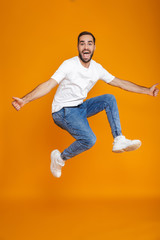 Fototapeta na wymiar Full length photo of unshaved guy in t-shirt and jeans jumping and having fun, isolated over yellow background