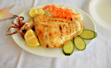 Grilled squid with carrots, onion, cucumber and lemon on a white plate