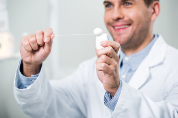 selective focus of dental floss in hands of smiling dentist