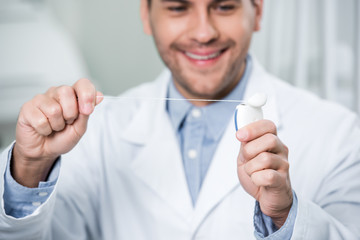 selective focus of dental floss in hands of cheerful dentist