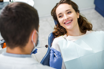selective focus of cheerful woman in braces during examination of teeth near dentist