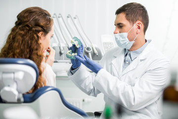 Fototapeta na wymiar selective focus of dentist in latex gloves showing teeth model near female patient