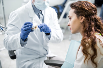 cropped view of dentist in latex gloves holding teeth model near female patient