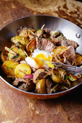 A delicious nourishing dinner of fried potatoes, meat, vegetables and soft chicken eggs served in a frying pan.
