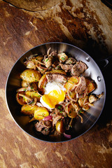 A delicious nourishing dinner of fried potatoes, meat, vegetables and soft chicken eggs served in a frying pan.