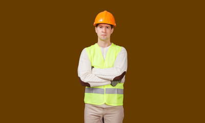 The man in a construction helmet and a vest, looks in the camera, hands are crossed