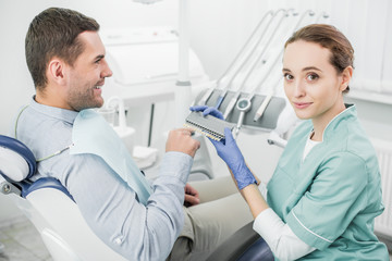 Obraz premium happy patient pointing with finger at teeth color palette near dentist