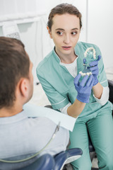 selective focus of beautiful dentist holding teeth model near patient