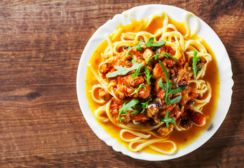 Sliced fried meat with vegetables and mushrooms in a sauce with bavette pasta in a plate on wooden table