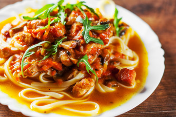 Sliced fried meat with vegetables and mushrooms in a sauce with bavette pasta in a plate on wooden table