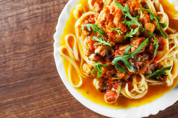 Sliced fried meat with vegetables and mushrooms in a sauce with bavette pasta in a plate on wooden table