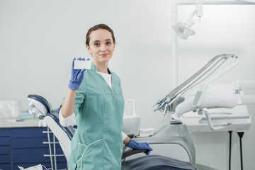 beautiful dentist holding blank card while standing in dental clinic