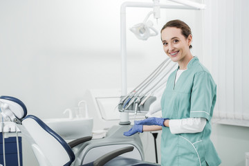 attractive dentist with braces on teeth smiling and gesturing in dental clinic