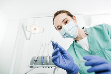 Fototapeta na wymiar selective focus of female dentist in mask and latex gloves holding dental instrument