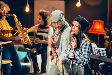 Band practice in home studio. Woman singing while rest of the band playing instruments.