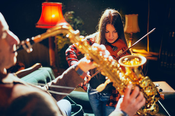Two talented musicians playing violin and saxophone. Home studio interior.
