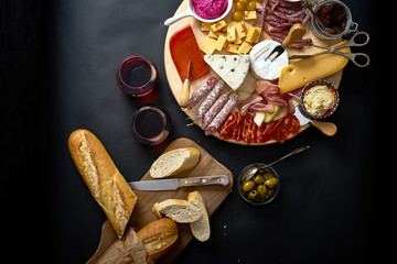 Antipasti board with cheese and meat snacks with red wine and baguette on board on black table
