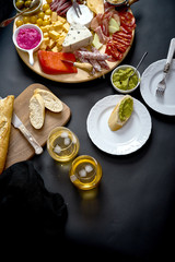 Antipasti board with cheese and meat snacks with white wine and baguette on board on black table
