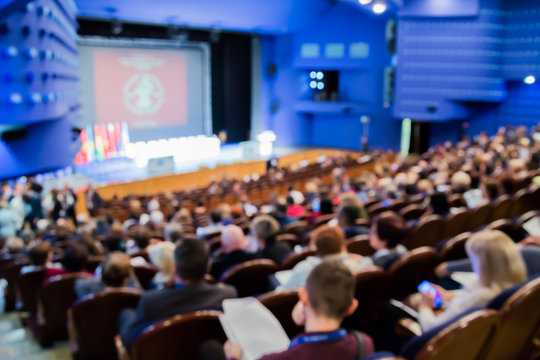 Defocused image. People in the auditorium. International conference. Flags of different countries on stage.