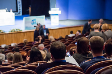 The audience in the auditorium. Conference or seminar. A stage with a podium and speakers. Defocused background. Bokeh effect.
