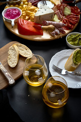Antipasti board with cheese and meat snacks with white wine and baguette on board on black table